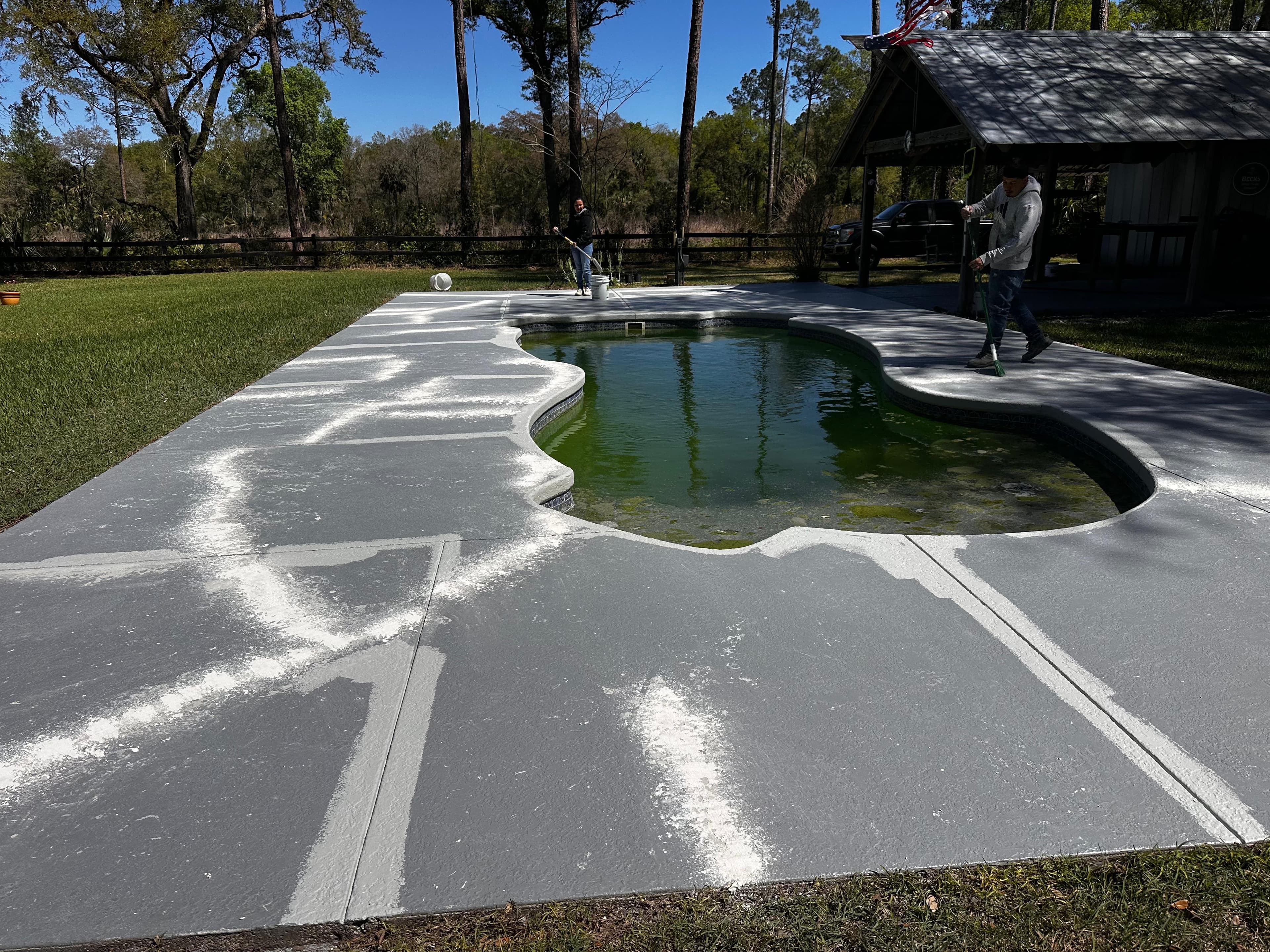 Two-man crew applying concrete deck coating around pool