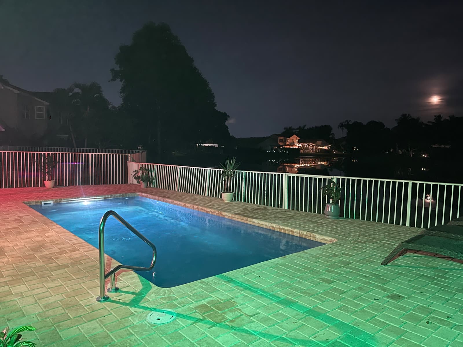 Finished Latham Delray fiberglass pool lit at night with a brick paver deck on a lakefront lot in West Palm Beach FL